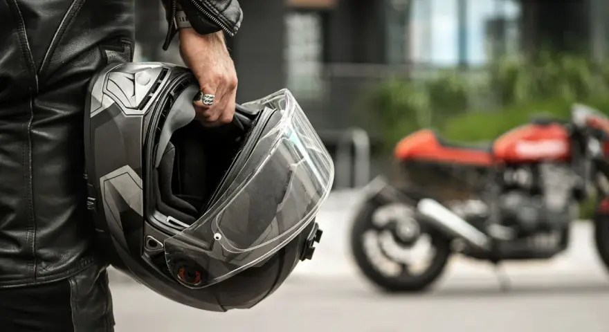 Motociclista con casco, simbolo di sicurezza e certificazione casco moto. Moto rossa sfocata sullo sfondo.