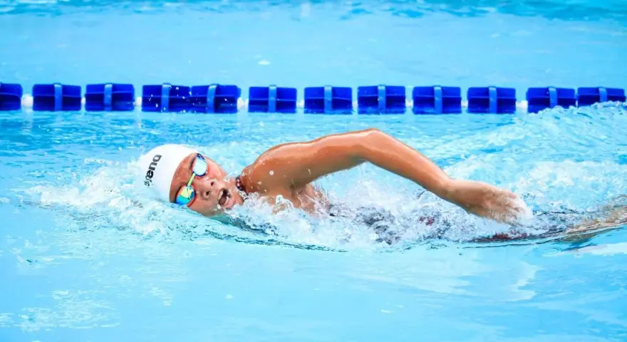 Un nageur concentré en pleine séance natation, la tête hors de l'eau, les bras en mouvement dans la piscine.