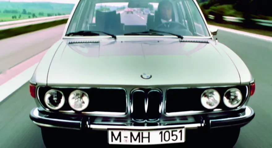 Srebrne BMW E3 z lat 70. jedzie po drodze.
