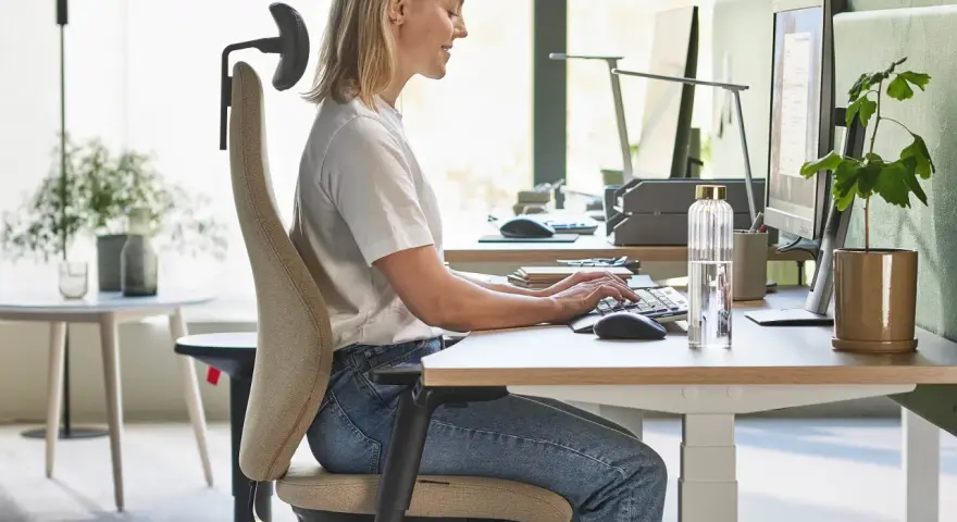 En kvinna sitter ergonomiskt vid ett skrivbord och arbetar vid datorn.