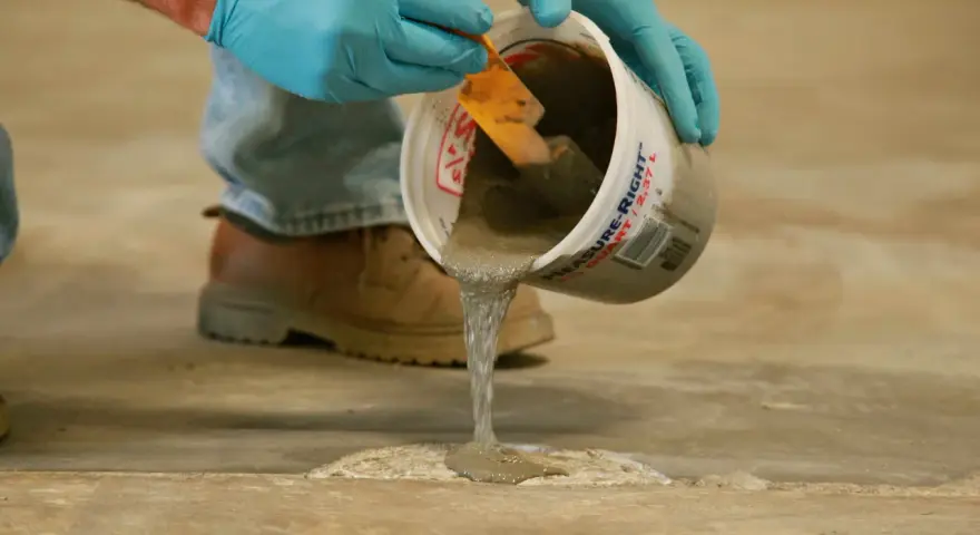 Man con guantes azules vierte hormigón líquido de un cubo para reparar el suelo. Aprende como hacer hormigón para suelo.
