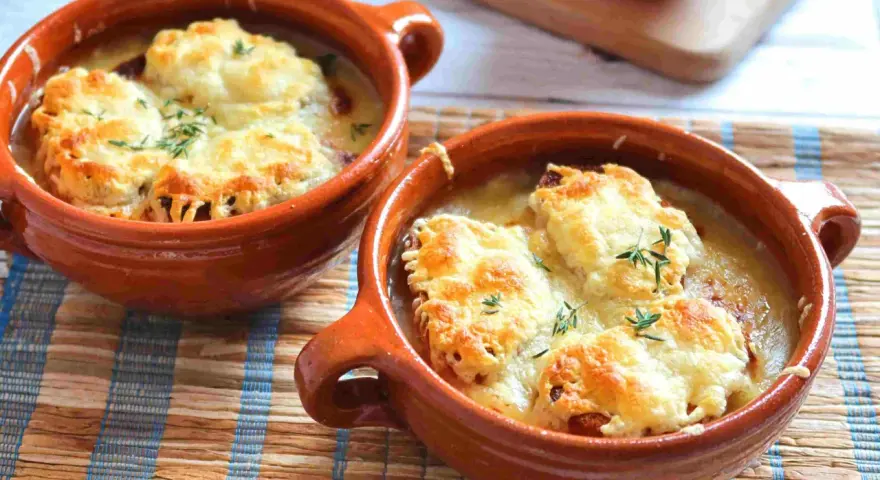Dos cazuelas de barro con sopa de cebolla gratinada con queso y hierbas.