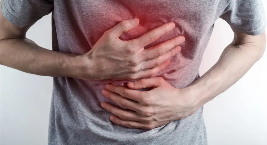 Osoba trzyma się za brzuch, odczuwając ostry ból w klatce piersiowej na środku. Czerwony obszar na koszulce sugeruje miejsce dolegliwości.
