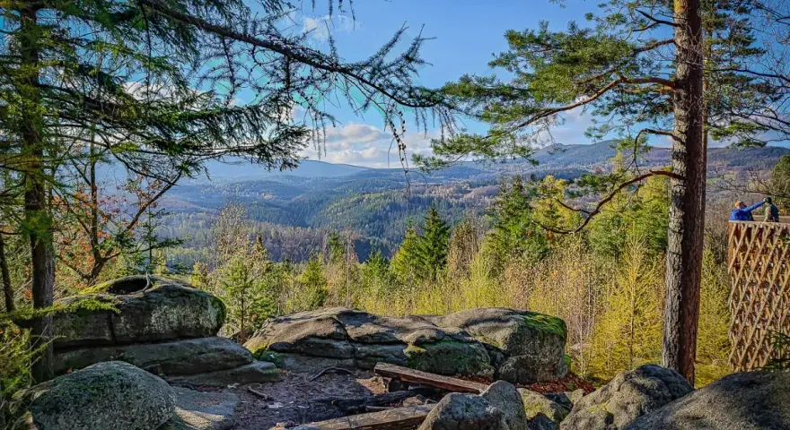 Kamienne skały i ławki na tle rozległej, leśnej panoramy Karkonoszy.