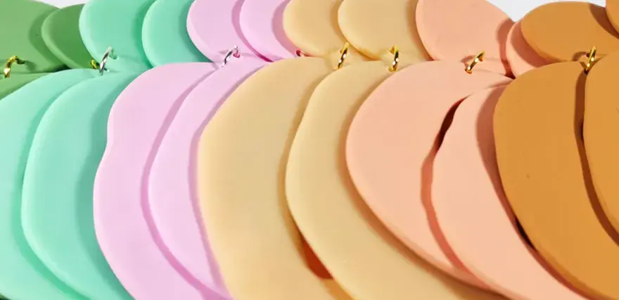 Fimolera smycken i pastellfärger, arrangerade i en mjuk kurva. Grönt, mintgrönt, rosa, beige och orange skapar en drömsk färgpalett.