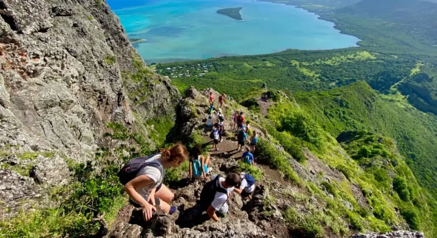 Grupa turystów wędruje po skalistym szlaku na Le Morne Mauritius, podziwiając zapierający dech w piersiach widok na turkusową lagunę i zielone wzgórza.