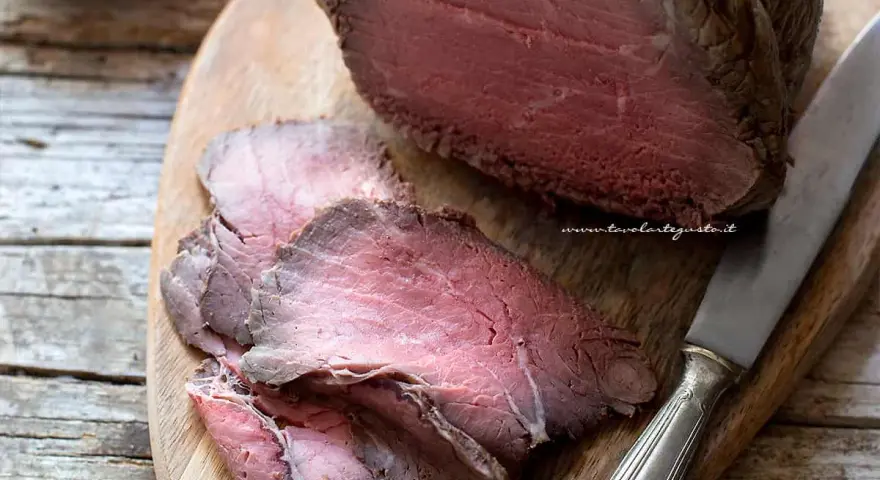 Roast beef ricetta classica: succulento arrosto affettato su tagliere di legno, pronto per essere gustato.