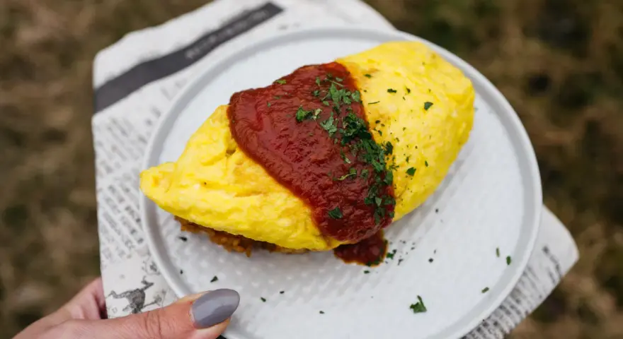 Pyszny omlet ryżowy polany sosem pomidorowym i posypany natką pietruszki, podany na talerzu.