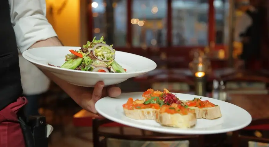 Un camarero experto demuestra cómo servir una mesa, presentando un plato de ensalada fresca y bruschettas.