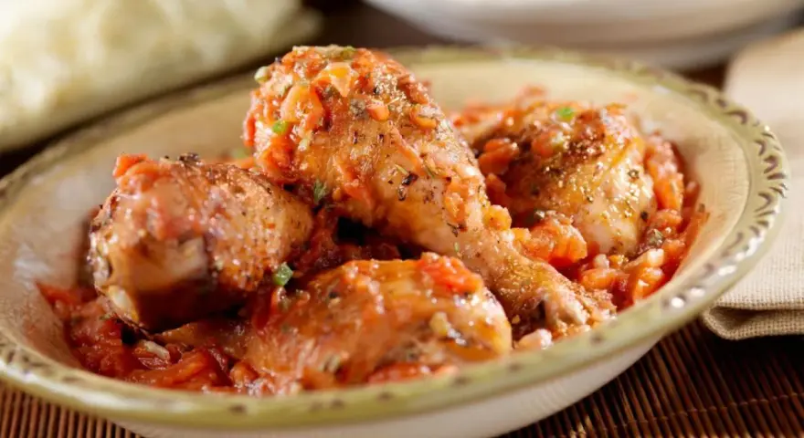 Pollo en salsa de tomate con hierbas, servido en un cuenco rústico.