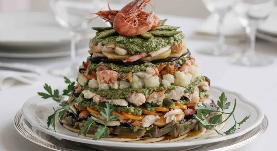 Un maestoso cappon magro a strati, con gamberi, verdure e salsa verde, guarnito con prezzemolo fresco.