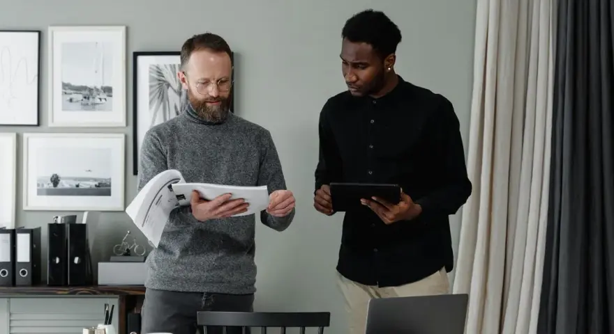 Two men review documents and a tablet, discussing the details of in-kind donation accounting.