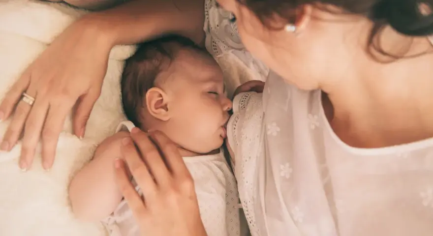 Delikatne karmienie noworodka. Mama czule tuli dziecko, które śpi, ssąc pierś. Wskazówki, jak wybudzić noworodka do karmienia, mogą być pomocne w takich chwilach.