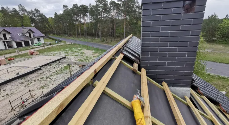 Budowa dachu: widok na drewniane łaty i komin. Wymiary kontrłaty są kluczowe dla stabilności konstrukcji.