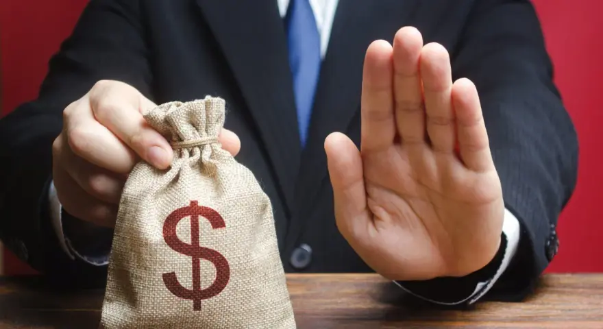 Syndyk nie zabiera świadczeń socjalnych. Mężczyzna w garniturze pokazuje worek z pieniędzmi i gestem dłoni odrzuca propozycję.