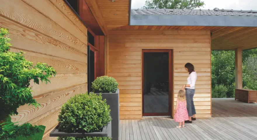 Piękna elewacja z drewna, której impregnacja zapewnia trwałość i naturalny wygląd. Kobieta z dzieckiem na tarasie.