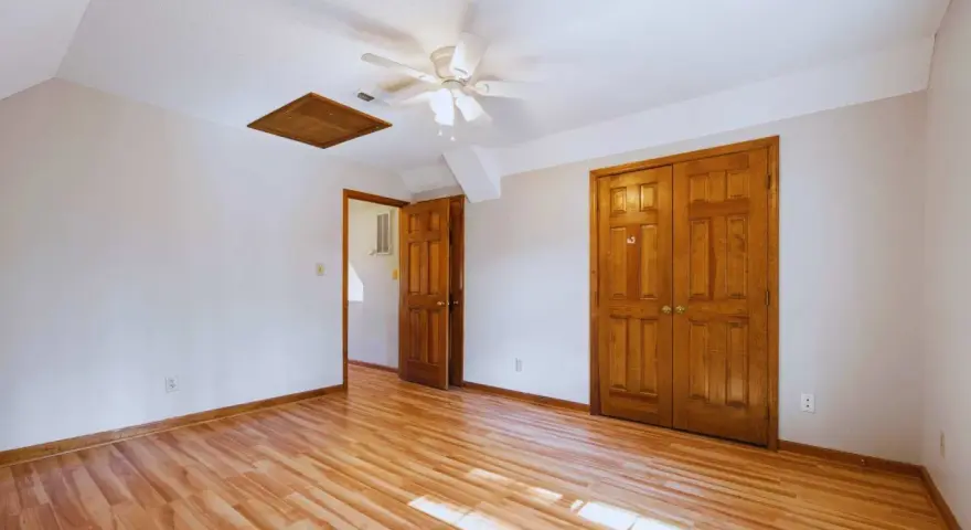 Habitación con suelo de madera clara y puertas de madera oscura, creando un bonito contraste. Un ventilador de techo ilumina el espacio.