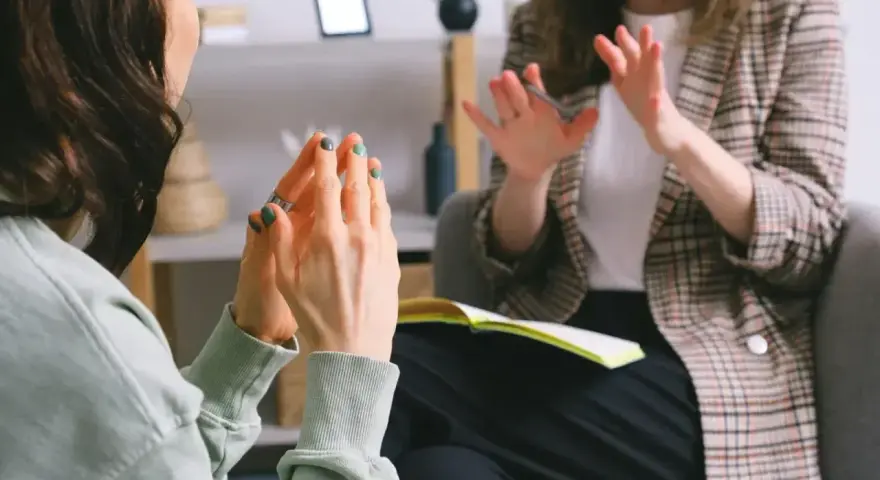 Dwie kobiety rozmawiają w gabinecie, jedna gestykuluje.