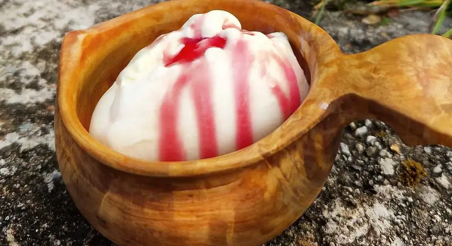 En skopa hemmagjord glass med röd sås i en träkopp, placerad utomhus på sten.