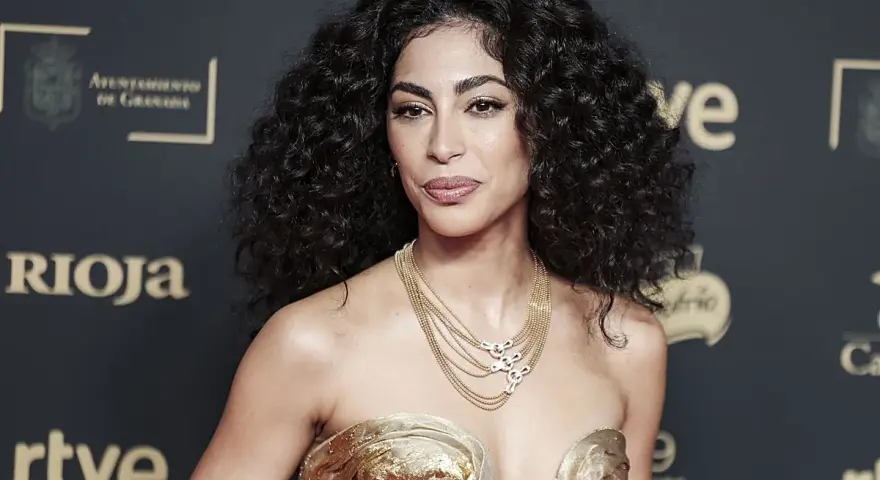 Mujer con espectacular pelo rizado, peinado con volumen y brillo. Luce un vestido dorado y un collar de cadenas.