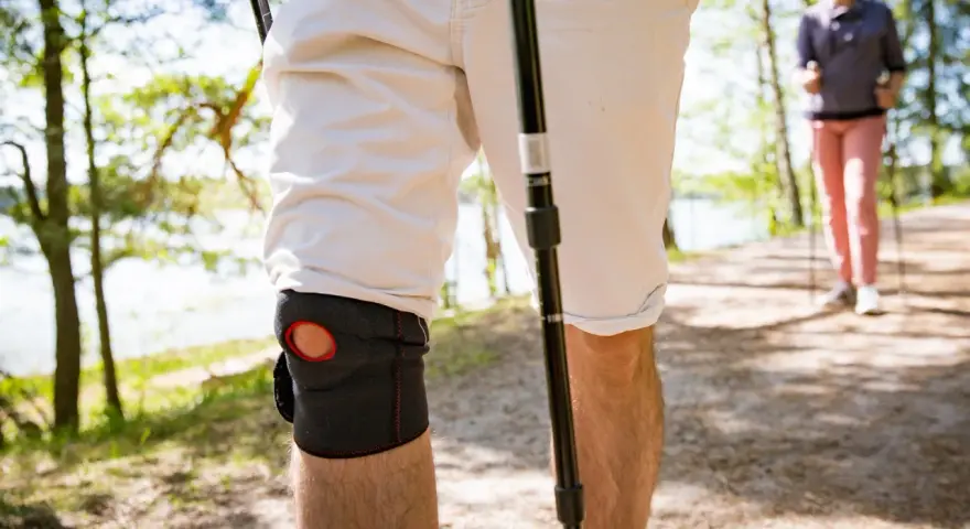 Mann mit Kniebandage beim Nordic Walking. Knieschmerzen beim Bergabgehen beeinträchtigen die Wanderung.