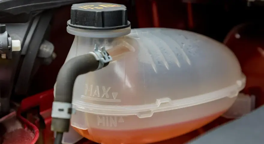A car's coolant reservoir with MAX and MIN lines. The orange coolant is between the lines, indicating the correct level. This image helps answer "what coolant does my car need.