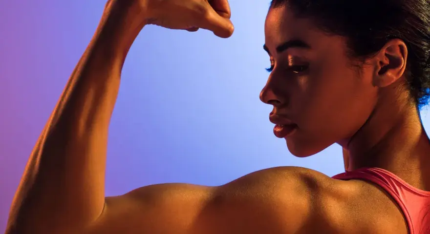 En kvinna flexar sin biceps, en demonstration av styrka och i muskelminnet.