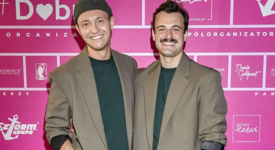 Kamil Krupicz i jego kolega pozują do zdjęcia na tle różowej ścianki z logotypami.