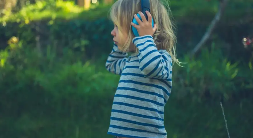 Ein Kind mit Kopfhörern im Freien, das die Welt der Klänge entdeckt. Diese Szene zeigt die Reizoffenheit bei Kindern, die sich neugierig auf neue Erfahrungen einlassen.