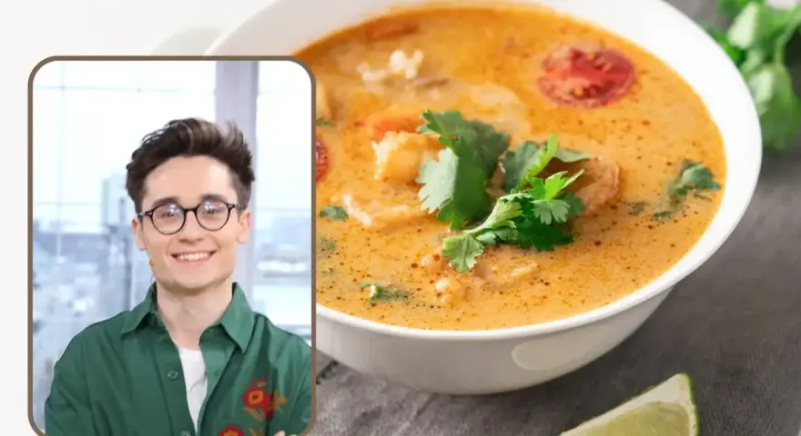 Uśmiechnięty mężczyzna w okularach prezentuje aromatyczną zupę tajską z krewetkami i pomidorkami, ozdobioną świeżą kolendrą.