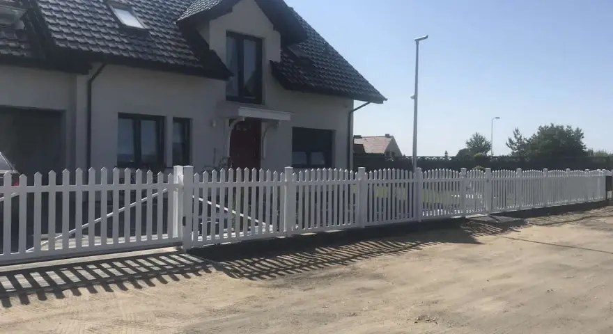 Biały płotek ogrodowy zrób to sam, idealnie otacza dom. Wygląda jak nowy, dodaje uroku posesji.