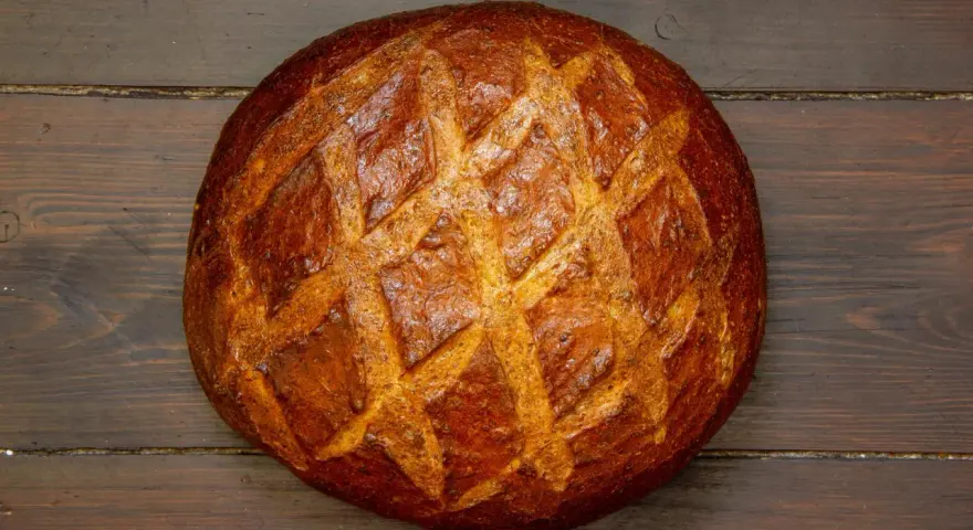 Ein **freigeschobenes Brot** mit knuspriger Kruste und Rautenmuster liegt auf dunklem Holz.
