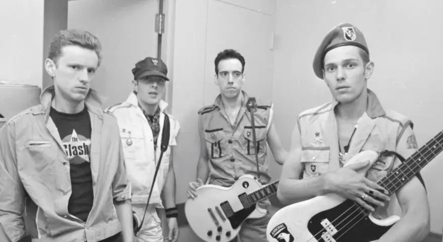 Les membres de The Clash posent avec leurs guitares. L'un porte un t-shirt "The Clash".