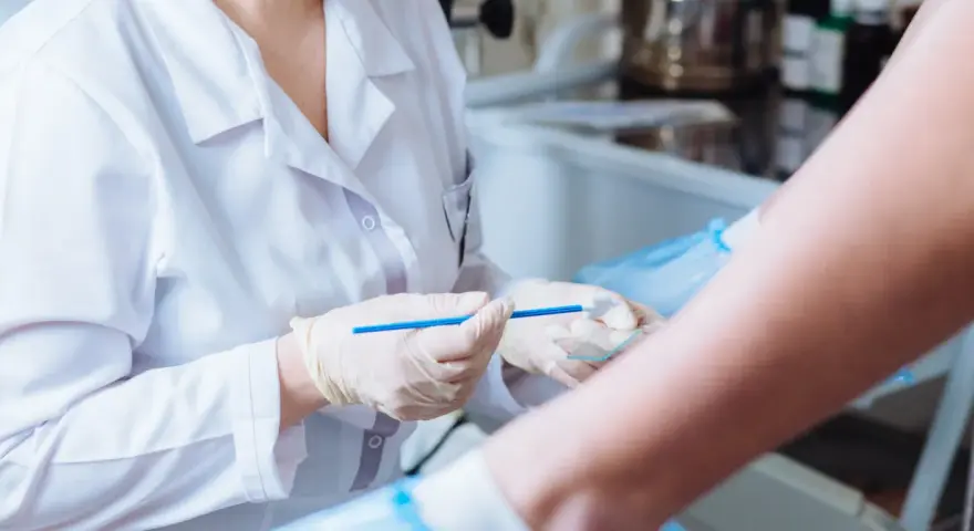 Lekarz w białym fartuchu i rękawiczkach trzyma szczoteczkę do cytologii płynnej nad szkiełkiem.