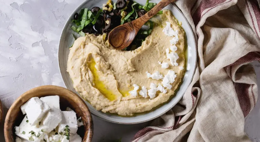 Pyszna pasta z ciecierzycy z fetą, oliwkami i ziołami, podana z serem feta w drewnianej misce.