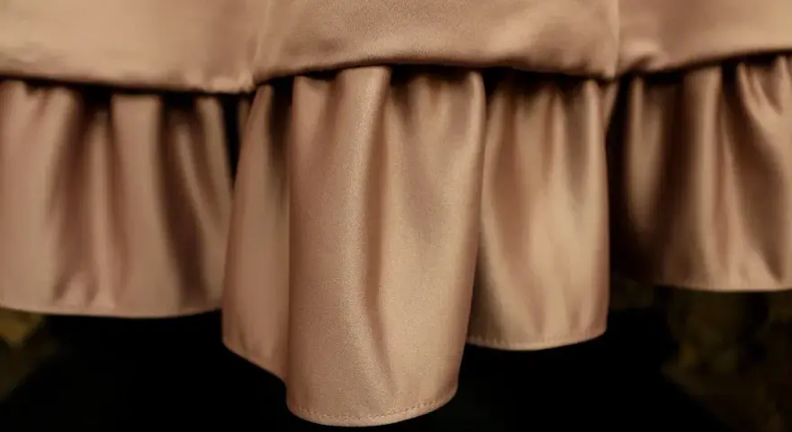 Delikatne marszczenia na **satynowym** materiale tworzą efektowną falbanę, dodając elegancji.