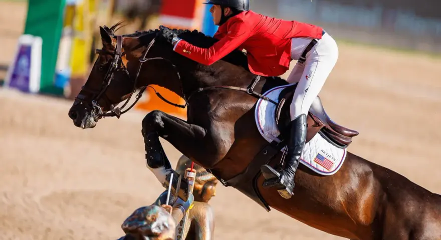 Le cheval Balou du Reventon saute un obstacle, son cavalier en veste rouge le guidant avec précision.