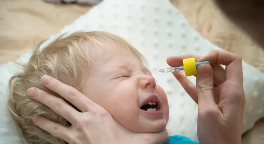 Ein Baby weint, während ihm N सेंटropfen verabreicht werden.