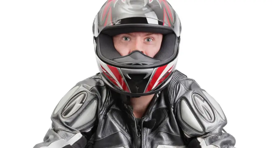 Occhi spalancati dietro un casco stretto, pronto per la corsa. La tuta in pelle grigia e nera completa il look da motociclista.