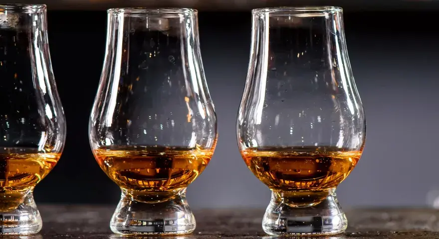 Drei Gläser mit bernsteinfarbenem Whisky stehen nebeneinander. Ein Blick auf die Whisky Kalorien für Genießer.