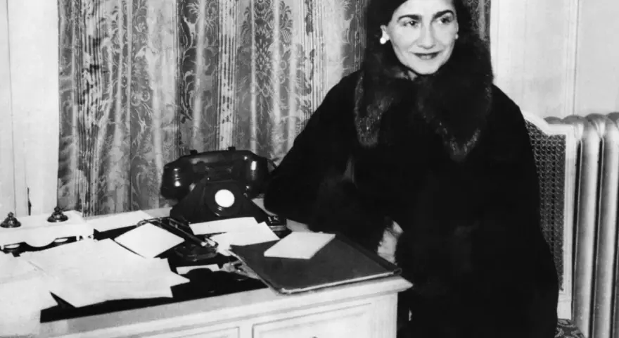 Coco Chanel, icona di stile, al suo scrittoio. La sua storia è fatta di eleganza e innovazione.