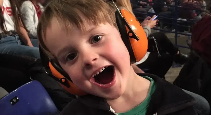 Un jeune garçon de 3 ans, avec un bouchon oreille enfant 3 ans, sourit à pleines dents, prêt pour le spectacle.