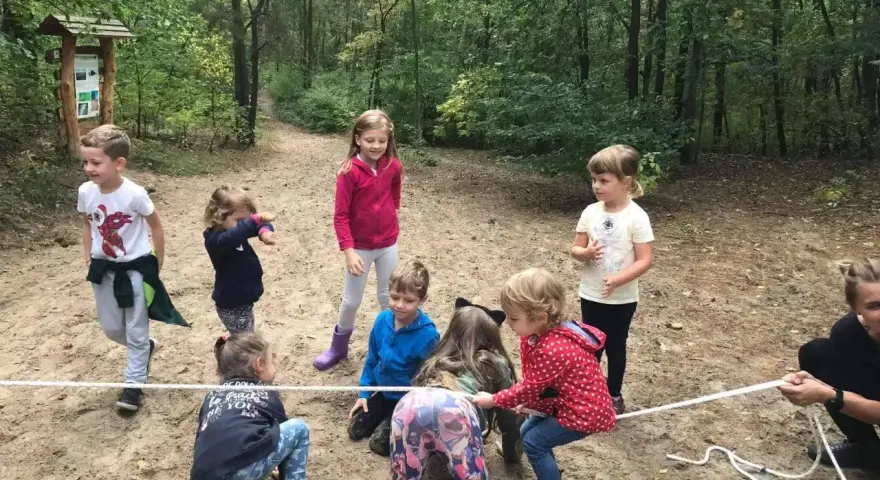 Grupa dzieci w wieku 6-12 lat bierze udział w przeciąganiu liny w lesie. Wszyscy świetnie się bawią!