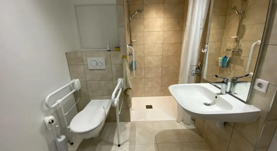 Salle de bain pmr avec douche à l'italienne, WC avec barres d'appui et lavabo. Confort et sécurité pour tous.