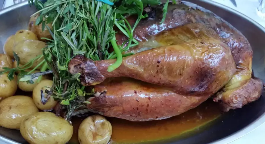 Pollo de Bresse asado, dorado y jugoso, acompañado de patatas pequeñas y hierbas frescas.