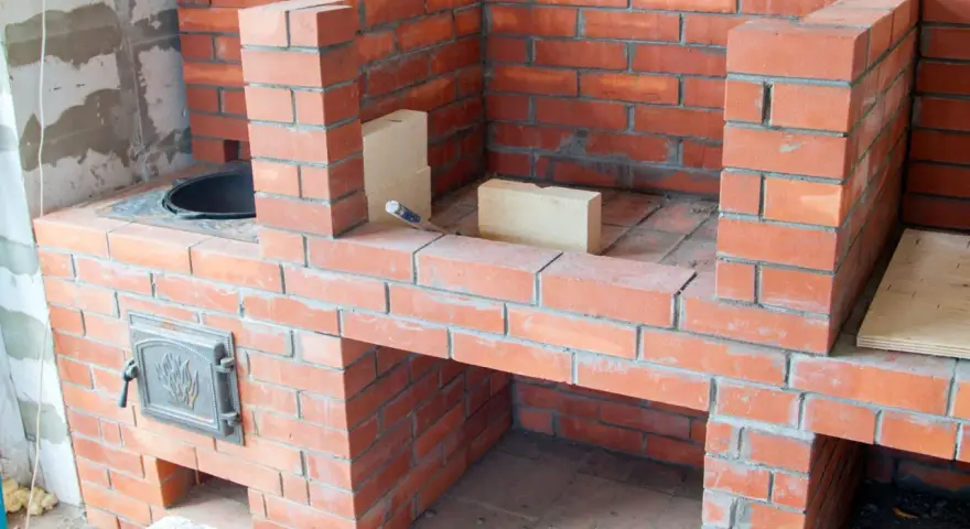 Construcción de chimeneas de obra de leña. Ladrillos rojos y mortero gris forman una estructura robusta, lista para encender el fuego.