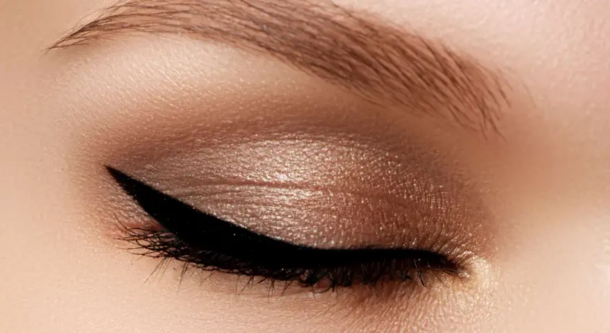 Occhio con trucco cat eyes, eyeliner nero definito e ombretto bronzo scintillante. Sopracciglio curato.
