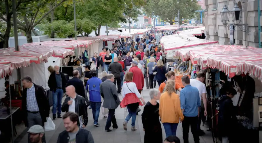 Menschen schlendern über einen belebten kunstmarkt berlin mit vielen Ständen und bunten Markisen.