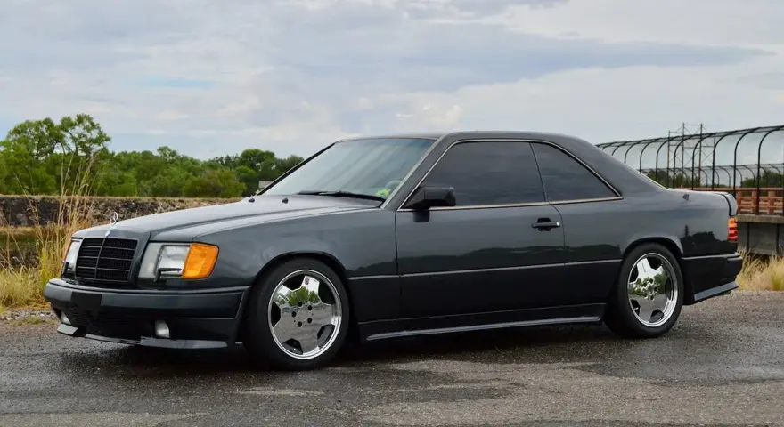 Ciemnoszary Mercedes "Hammer" coupe z przyciemnianymi szybami i chromowanymi felgami stoi na mokrej drodze.