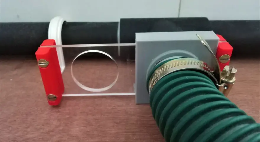 A 3d printed blast gate with a clear sliding mechanism and a green hose attached.